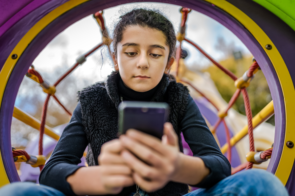 Little girl playing on mobile phone instead of enjoying the Park Little girl playing on mobile phone instead of enjoying the Park